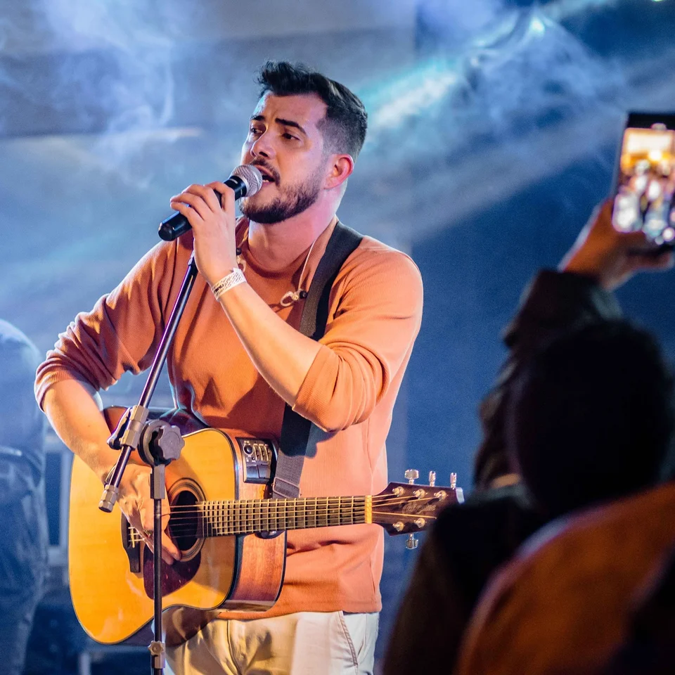 Gui Rosário cantando e tocando violão sob a iluminação azul do palco