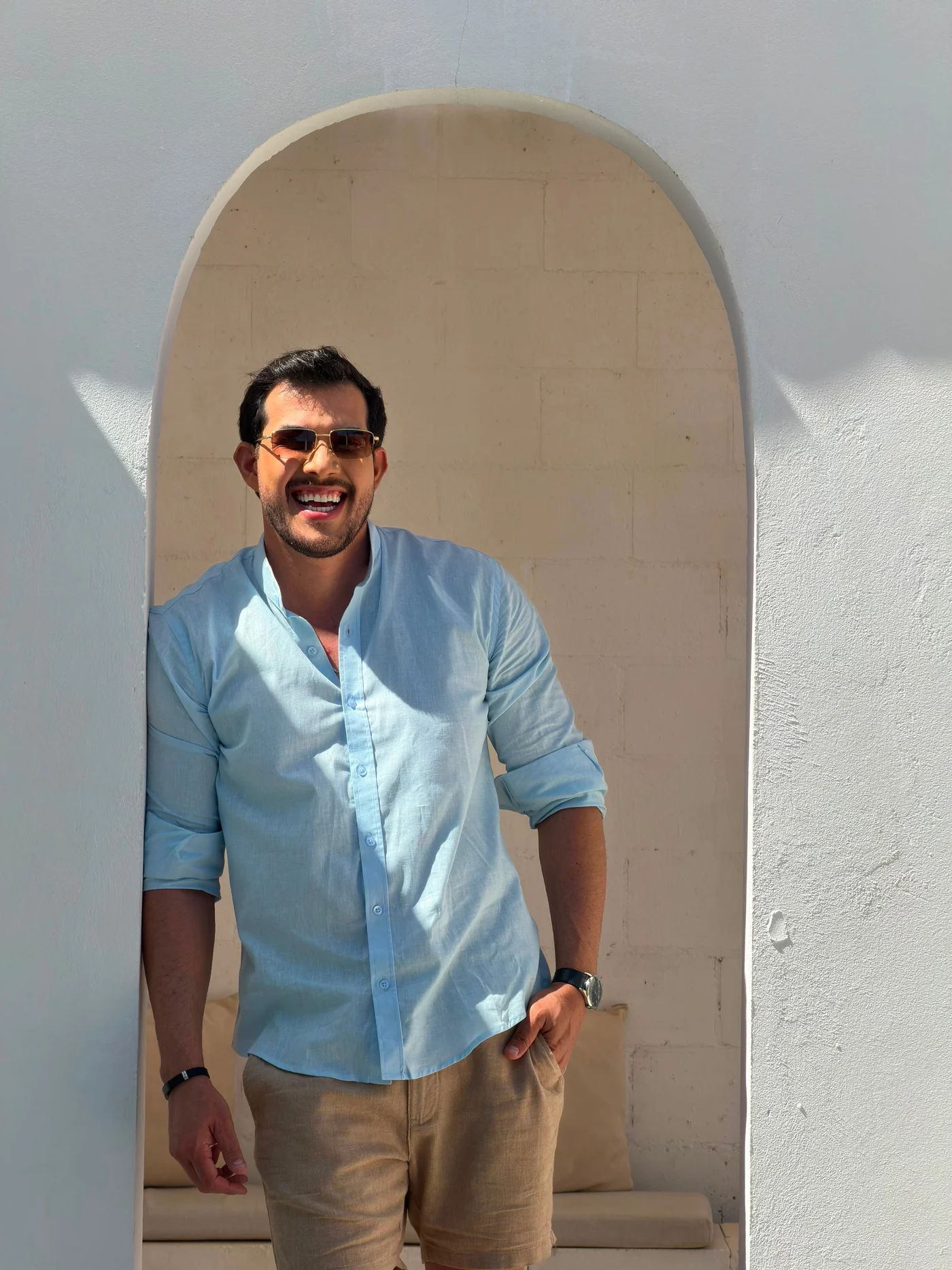 Gui Rosário sorrindo, de camisa azul, diante de um arco
